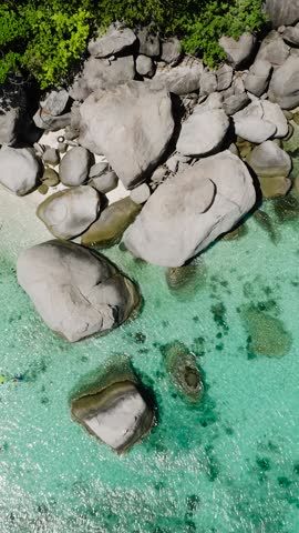 Large rocks scattered in shallow turquoise water near lush greenery along the coastline under sunny skies. Koh Tao, Thailand.