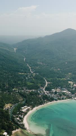 Tropical bay surrounded by lush green mountains and a small village on the coastline. Ko Pha Ngan, Thailand.