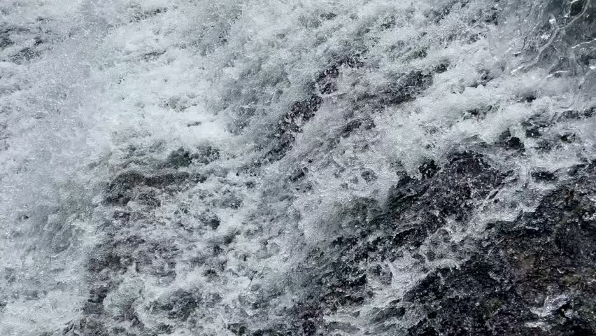 Water flows rapidly in a natural tropical river with a black rocky riverbed. Rapid river flow with black rock steps