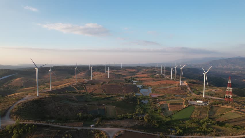 Aerial drone shot flying outdoors above the wind turbine field. Landscape of the windmill power turbines farm generating clean renewable energy for sustainable development at sunset.