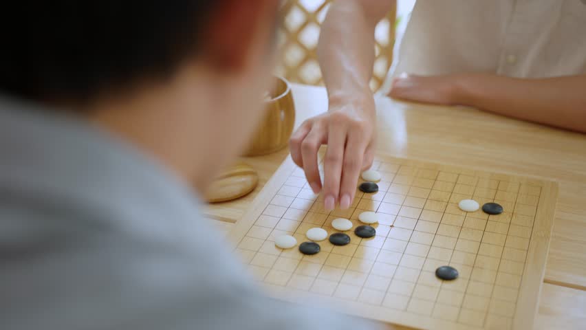 Close up of young men play board game Go during competition in community. Attractive two male friend players participate in traditional asian chinese board game match on table in the club house center