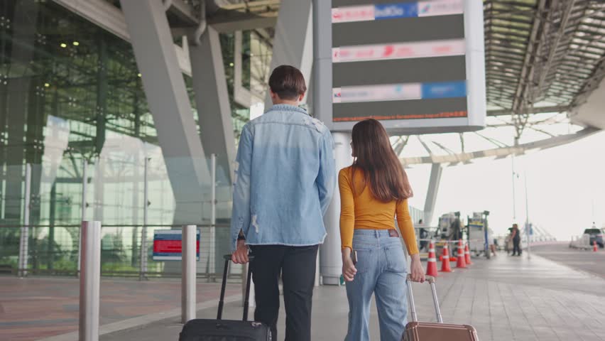 Asian young couple passenger walk in airport terminal to boarding gate. Attractive man and woman friends tourist feel happy and excited for going travel abroad by airplane for holiday vacation trip.