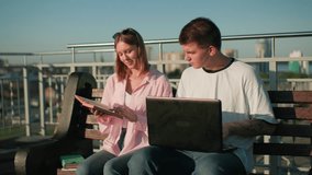 High school students study outdoors; male focused on laptop, female showing something in book against background with iron railing - Powered by Shutterstock - Get 15% off with code: PIKWIZARD15