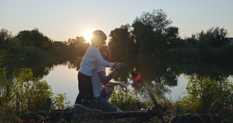 Father with Son Spend Together Happy Evening Time on Nature Watching Sunset Above Lake. 4K 10-bit