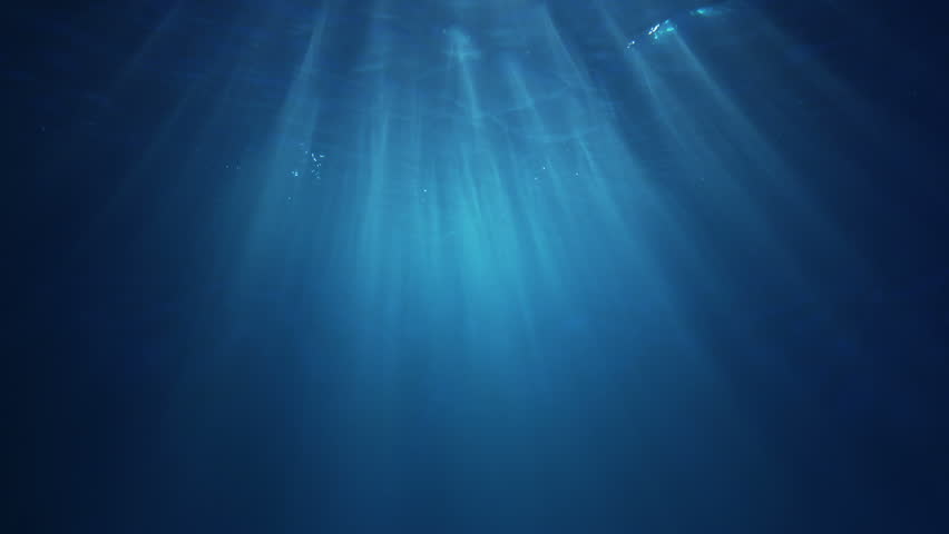 Light filtering down through blue water. Underwater sunlight in deep sea. Sunlight viewed from blue abyss, slow motion. Underwater sunlight shining deep under water with ripples on wave surface.