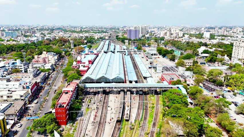 This aerial shot captures a comprehensive view of Chennai Railway Station, showcasing its extensive network of tracks and platforms. Several trains are visible on the tracks, while pedestrian bridges