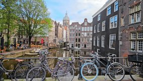 Bicycles parked on a bridge overlooking a picturesque canal in Amsterdam, surrounded by historic buildings. A large tree, boats, and outdoor cafes enhance the charm of the scenic view - Powered by Shutterstock - Get 15% off with code: PIKWIZARD15