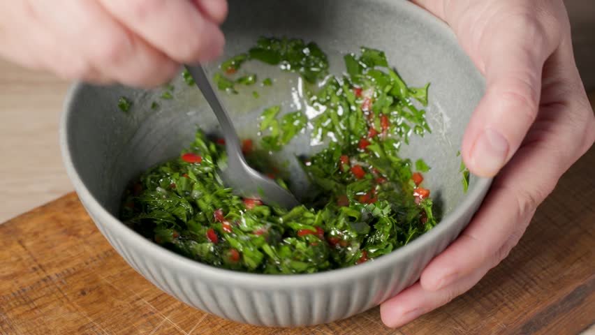 chef mix oil in a bowl of parsley chili salad for making healthy vegan chimichurri sauce in home kitchen, food closeup