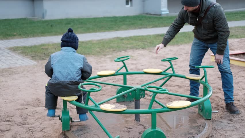 Father and son walking on urban playground. Handsome middle-aged man with toddler boy spending time together. Family, dad and his child playing on play area. City life. Children