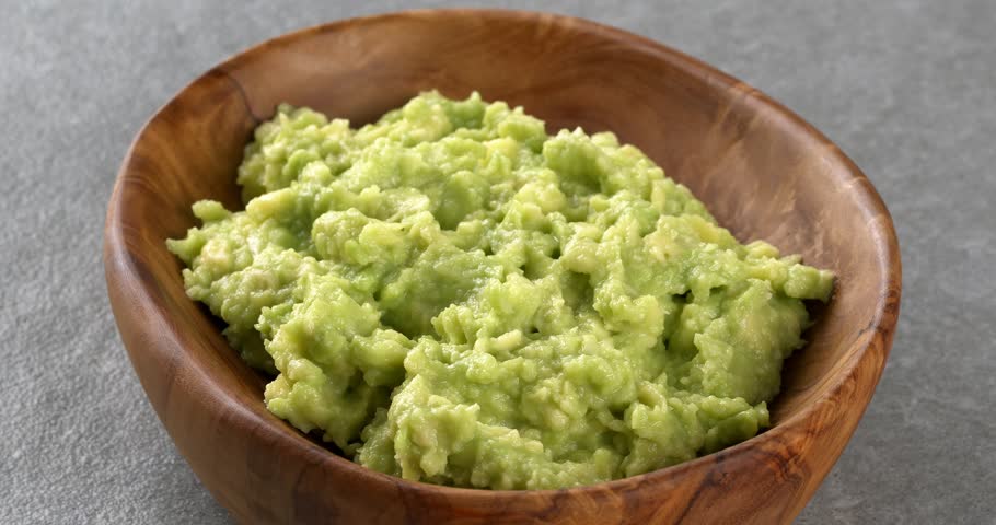 Guacamole in wooden bowl. Close-up footage on the rotating table.