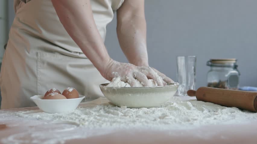 The cook in the bakery kneads the dough with his hands and begins to prepare the bread and pasta using traditional methods. Slow motion.