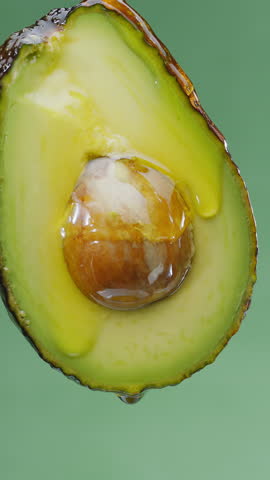 Oil is dripping down from cut in half avocado fruit. Conceptual slow motion vertical template.