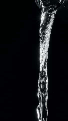Pure water is being poured out from a glass bottle on black background. Transparent water flow. Slow motion vertical template.
