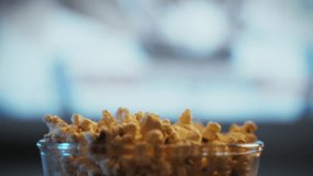 A hand extends toward a bowl of popcorn as a movie plays in the background, creating a relaxed atmosphere in a cozy living room - Powered by Shutterstock - Get 15% off with code: PIKWIZARD15