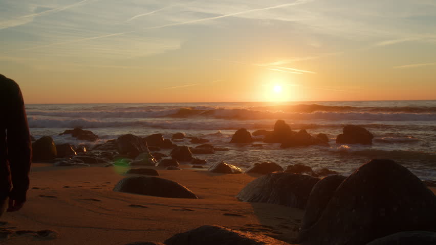 Lonely young man walking towards a sunset on the beach. Slow motion