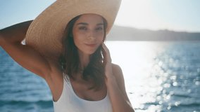 Luxurious woman relaxing on ocean shore wearing straw hat closeup. Stylish model posing summer sunlight in front bright sea water surface. Happy tourist girl standing tropical beach in white swimsuit. - Powered by Shutterstock - Get 15% off with code: PIKWIZARD15