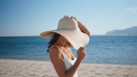 Carefree traveler walking sea beach in stylish straw hat closeup. Luxurious woman posing at beautiful sunny seashore strolling on sand. Happy brunette lady looking camera in front blue marine horizon. - Powered by Shutterstock - Get 15% off with code: PIKWIZARD15