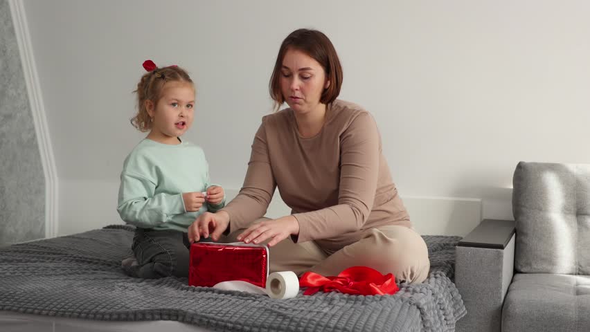 Happy young mother and a little daughter pack gifts together for Valentine