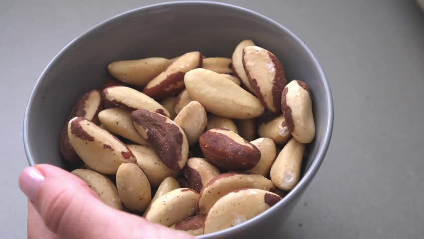 Brazil nut in a bowl, eating female hand.