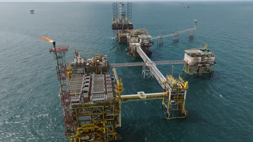 Sweeping aerial of huge offshore processing platform with multiple gas flares, oil industry
