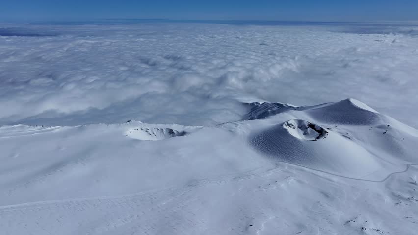 Etna summit area in winter with a landscape with snow covering craters and volcanic rocks. The smoke from the eruptions creates a unique atmosphere. Above the clouds. Etna cable car.
