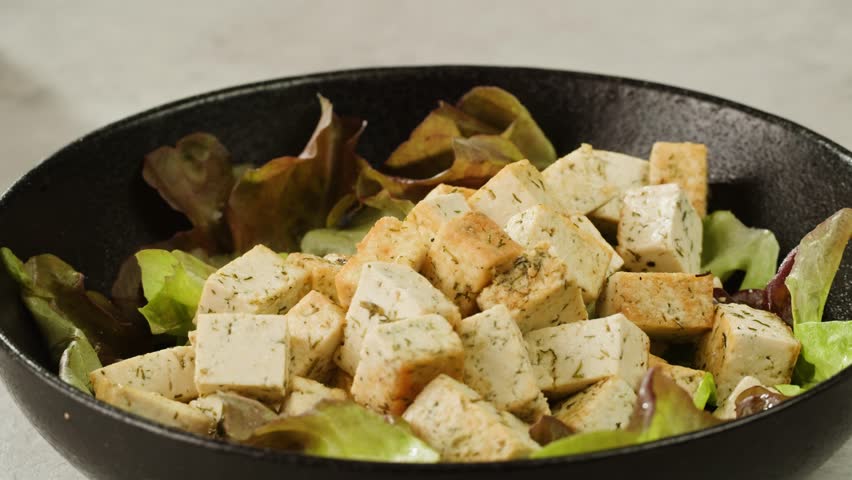Fried tofu with sesame seeds and spices on cast iron pan, cooking japanese salad. Healthy ingredient for cooking vegan vegetarian diet food. Roasted tofu over black background.
