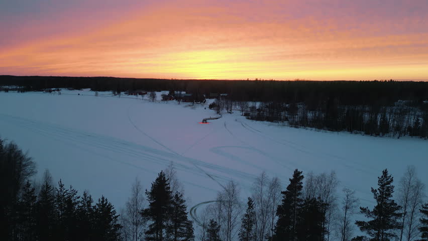 Winter ice bath and sauna location, frozen lake in Northern Finland, wide aerial view shot at sunset