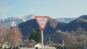 Give way street sign for vehicles driving in street with mountains in background. Yield traffic sign for cars in New Zealand town in suburban road surrounded by natural view of mountains and trees - Powered by Shutterstock - Get 15% off with code: PIKWIZARD15