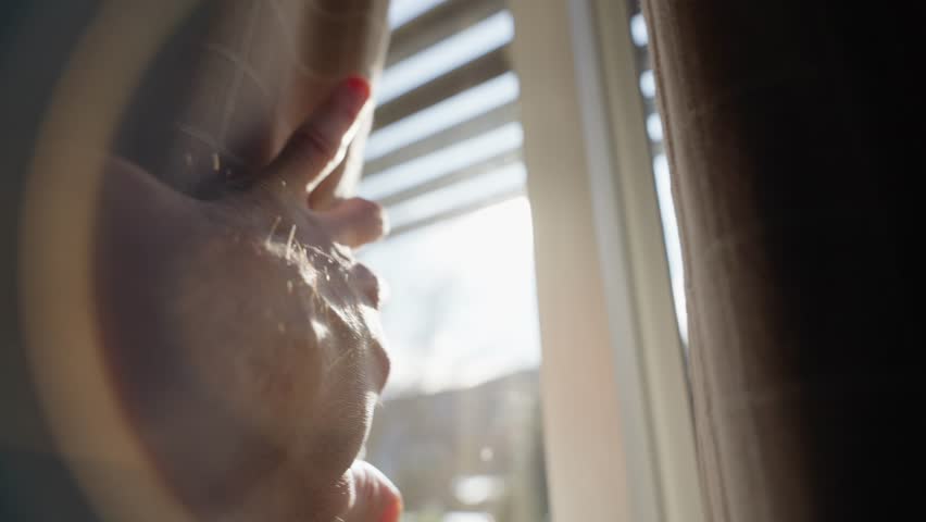 Hand slowly reaching towards a window curtain and open it to reveal sunlight. Dark room as hand of a man pushes heavy drape to let the sunlight shine inside. Bright sunny day outside. Hope and energy