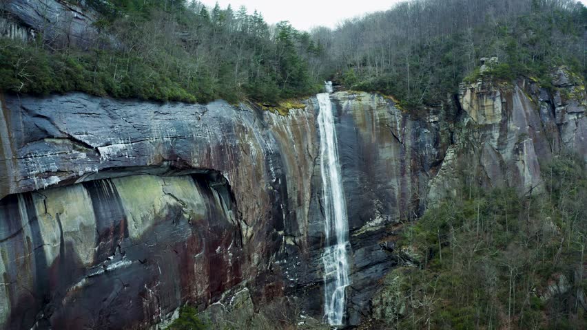 Scenic aerial pullback of Hickory Nut Falls of Chimney Rock forested mountains and rocky cliffs, North Carolina