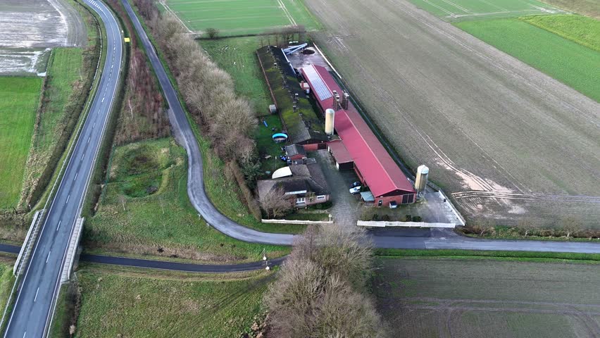 Long farmers house with red tile and solar panel in american countryside. Car driving on rural intersection road. Frosty and cold winter day in USA. Aerial top down flyover. Silo storage in garden.