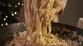 Chef in restaurant kitchen uses tongs to mix fettuccine pasta, mushrooms, and creamy white sauce on hot pan, creating an appetizing and nutritious dish. - Powered by Shutterstock - Get 15% off with code: PIKWIZARD15