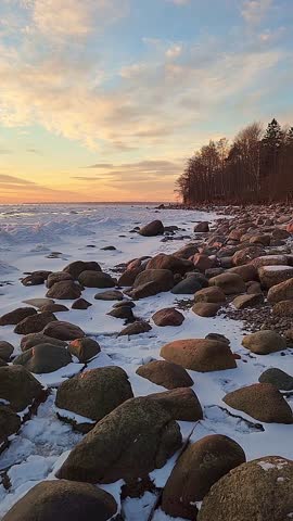 Winter landscape. Panoramic view of beautiful sunset on bay. List clouds over water in bright light. Ice, snow and rocks on coastline. Setting sun is reflected in sea. High quality footage
