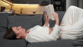 A woman reads a book while lying on the sofa at home. - Powered by Shutterstock - Get 15% off with code: PIKWIZARD15