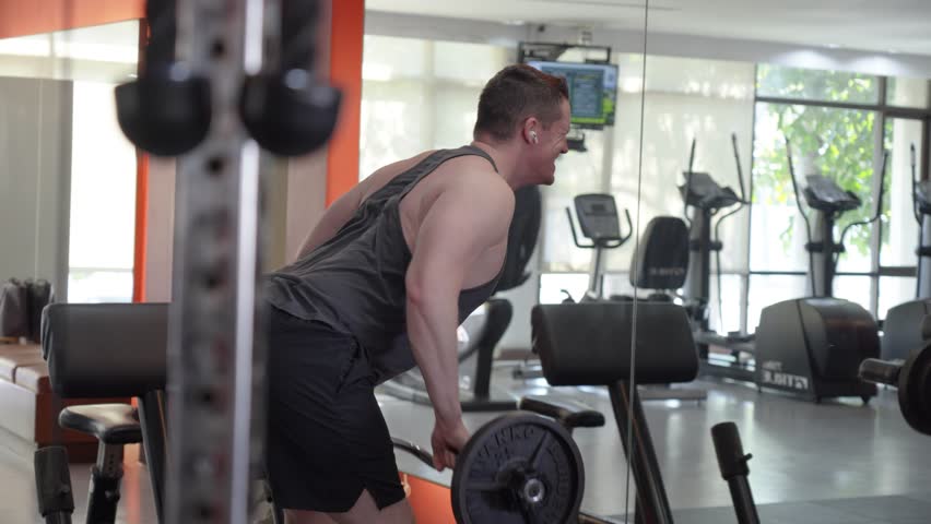 A man performing a barbell bent-over row in a gym. Focused on back and arm strength, this workout highlights the concept of weight training, muscle development, and physical fitness.