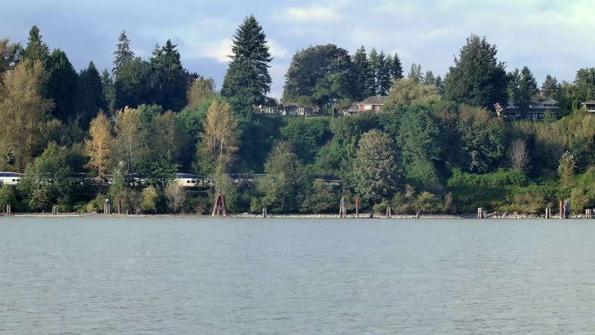 Train Traveling On A Railway Line Along The River. - wide shot