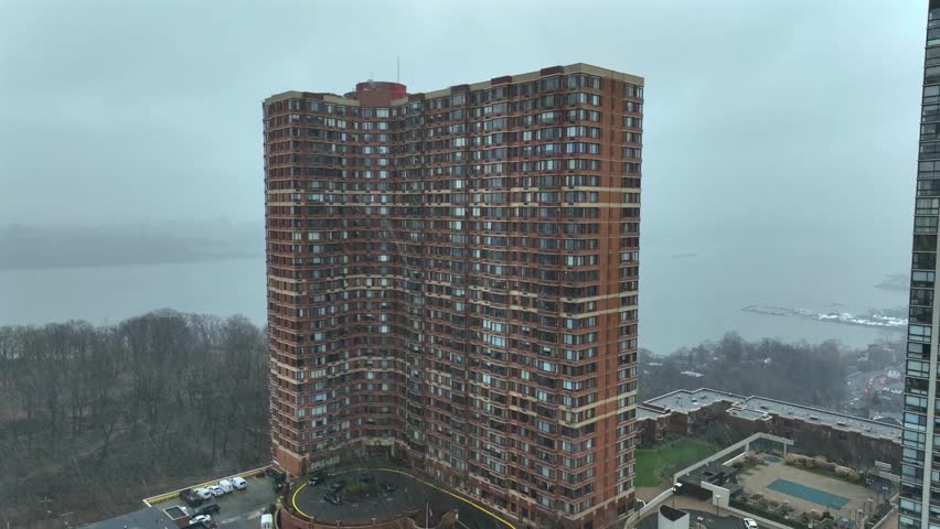Residential apartment block in Fort Lee during snowy storm in winter. Hudson River in distance. Aerial wide shot. Ancient apartment tower with cheap homes.