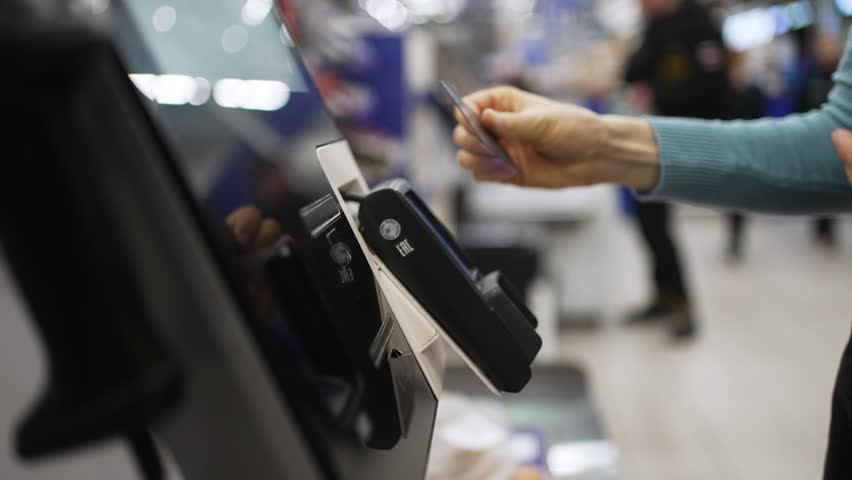 Female shopper performing contactless payment using credit card at self-service kiosk, showcasing modern, efficient retail technology and cashless transaction method