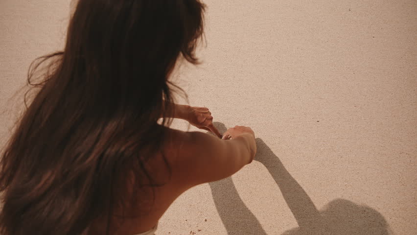 Woman drawing a heart in the sand on a sunny beach