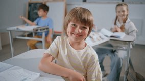 Portrait cheerful pupil boy looking camera at school. Happy smiling kid sitting class room posing with classmates at background. Funny little child enjoying lesson listening teacher. Education concept - Powered by Shutterstock - Get 15% off with code: PIKWIZARD15