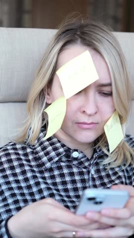 Tired exhausted young business woman working at home with many stickers task inscriptions on the face. Freelancer girl busy occupation feels sad boredom overworked multitasking. Panic attack, deadline