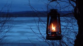 A kerosene lantern hangs on a tree branch and burns with an orange flame. Lantern on the background of the evening natural landscape on the shore of the lake. - Powered by Shutterstock - Get 15% off with code: PIKWIZARD15