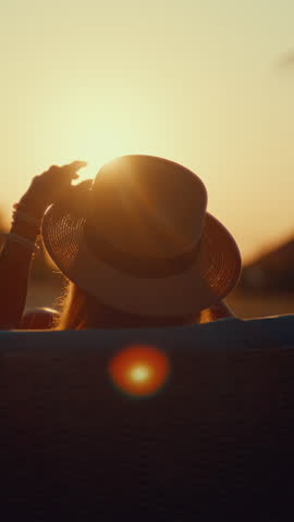 Relaxed woman admiring sunset, back view of lady lying on lounger, back view silhouette, enjoy summertime. Female person traveling to sea or ocean in summer vacation, backlit shot, calm contemplation