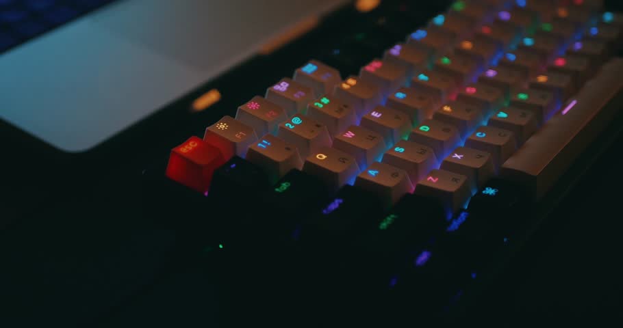 Close up of professional mechanical keyboard with colorful LED backlight in multiple colors. Advanced technology for gaming and developer workflows. Hands typing on keyboard