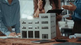 Professional architects collaborating over building scale model, reviewing blueprints and digital plans on wooden table, analyzing urban design project in modern workplace setting - Powered by Shutterstock - Get 15% off with code: PIKWIZARD15