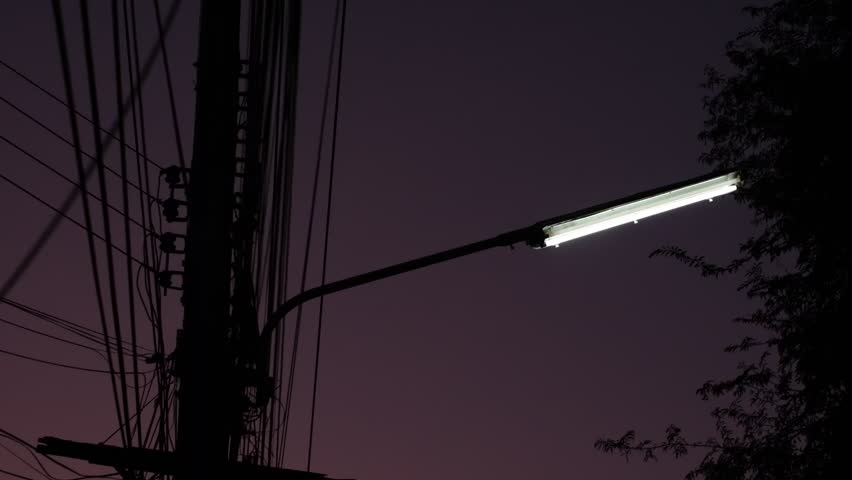 A street light is lit up in the dark. The light is on a pole and is shining brightly. The sky is dark and the street is empty