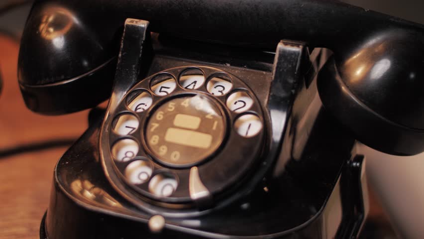 Pan shot focusing on a vintage rotary dial telephone in warm ambient light