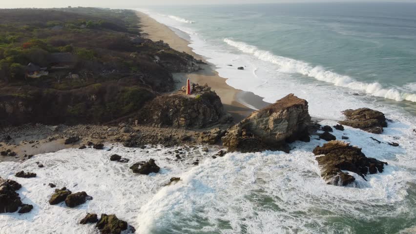 Aerial View of a Lighthouse on Scenic Coastal Cliff with Waves Crashing Against Rocky Shoreline