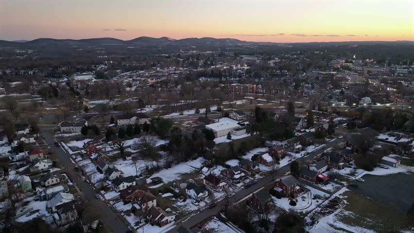 Snowy residential area with houses and homes during sunset time. Aerial descend wide shot. Quiet and peaceful landscape of small town in USA.