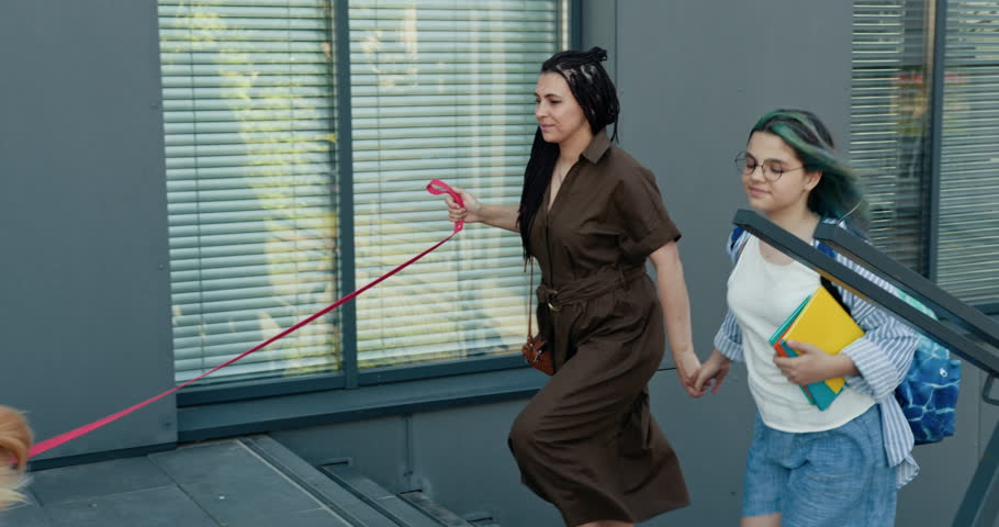 Modern family moment with mother and teenage daughter walking to school. Diverse female running late for class, carrying books and backpack. Emphasizes family bond, everyday routines, and city life.